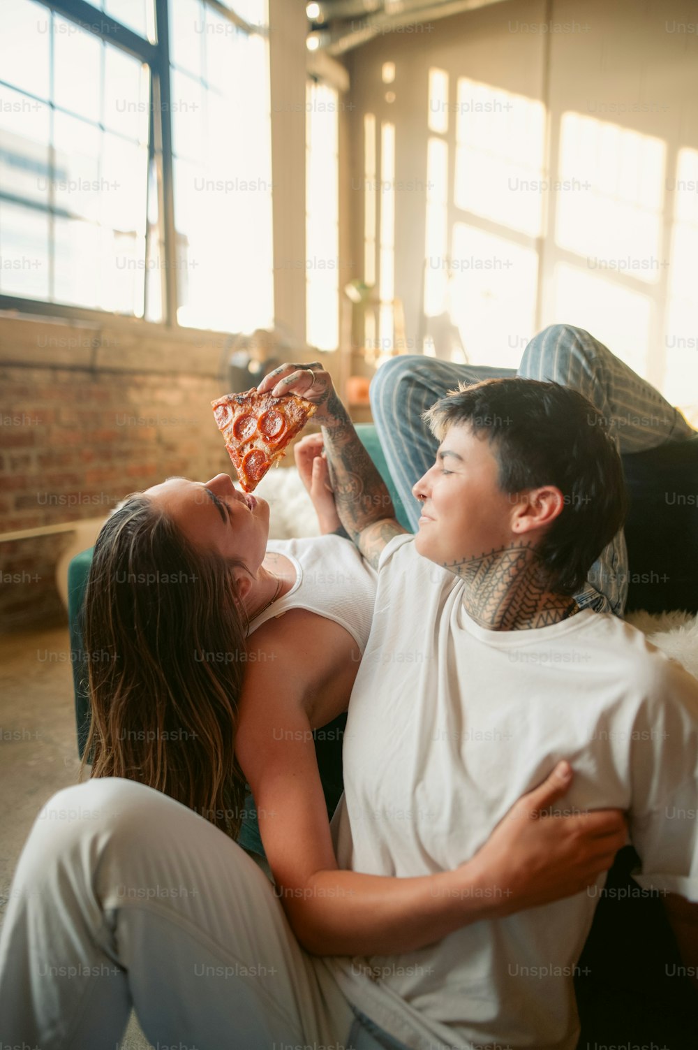 a man and a woman laying on a couch eating pizza