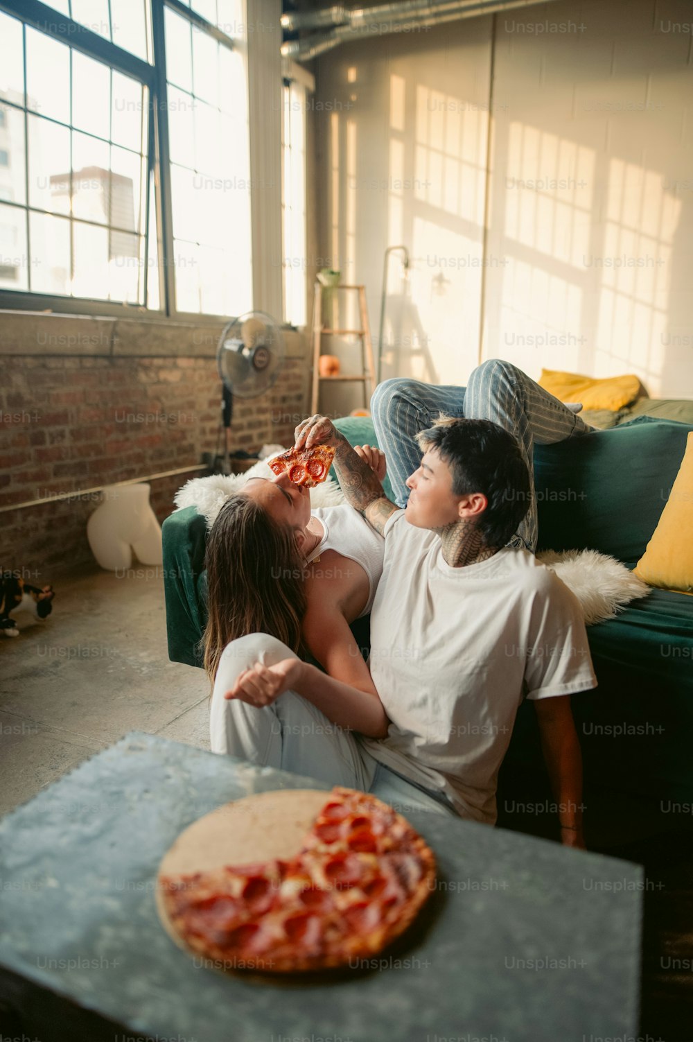 a man and woman sitting on a couch next to a pizza