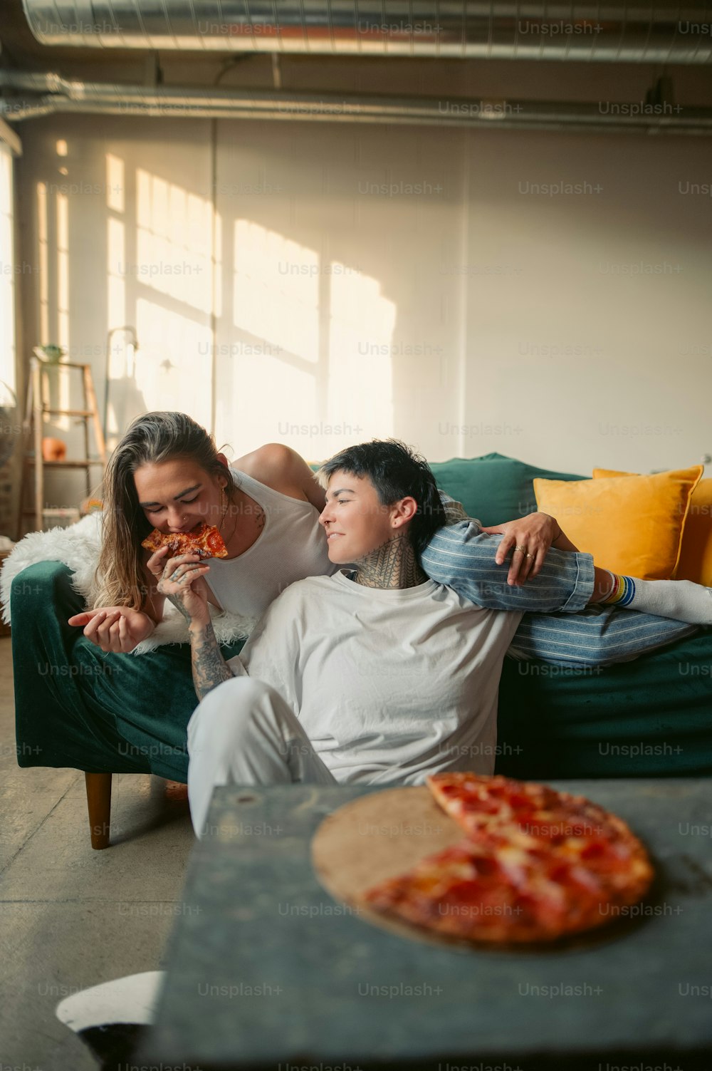 a man and a woman sitting on a couch eating pizza