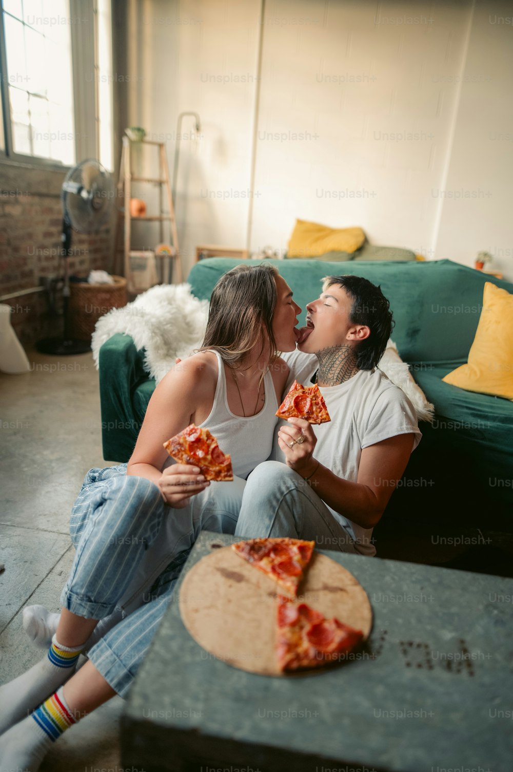 a man and woman sitting on a couch eating pizza