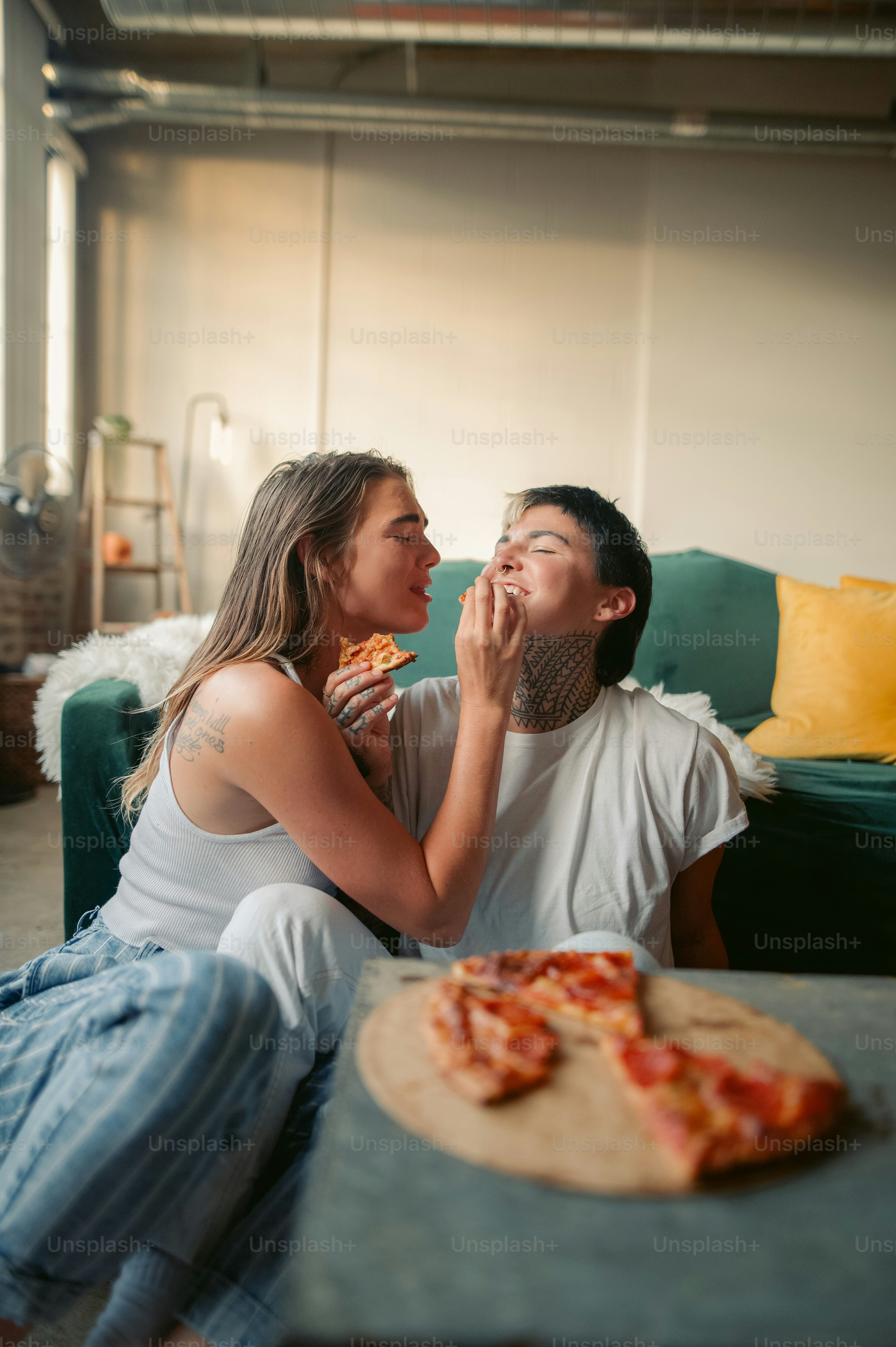 a man and woman sitting on a couch eating pizza