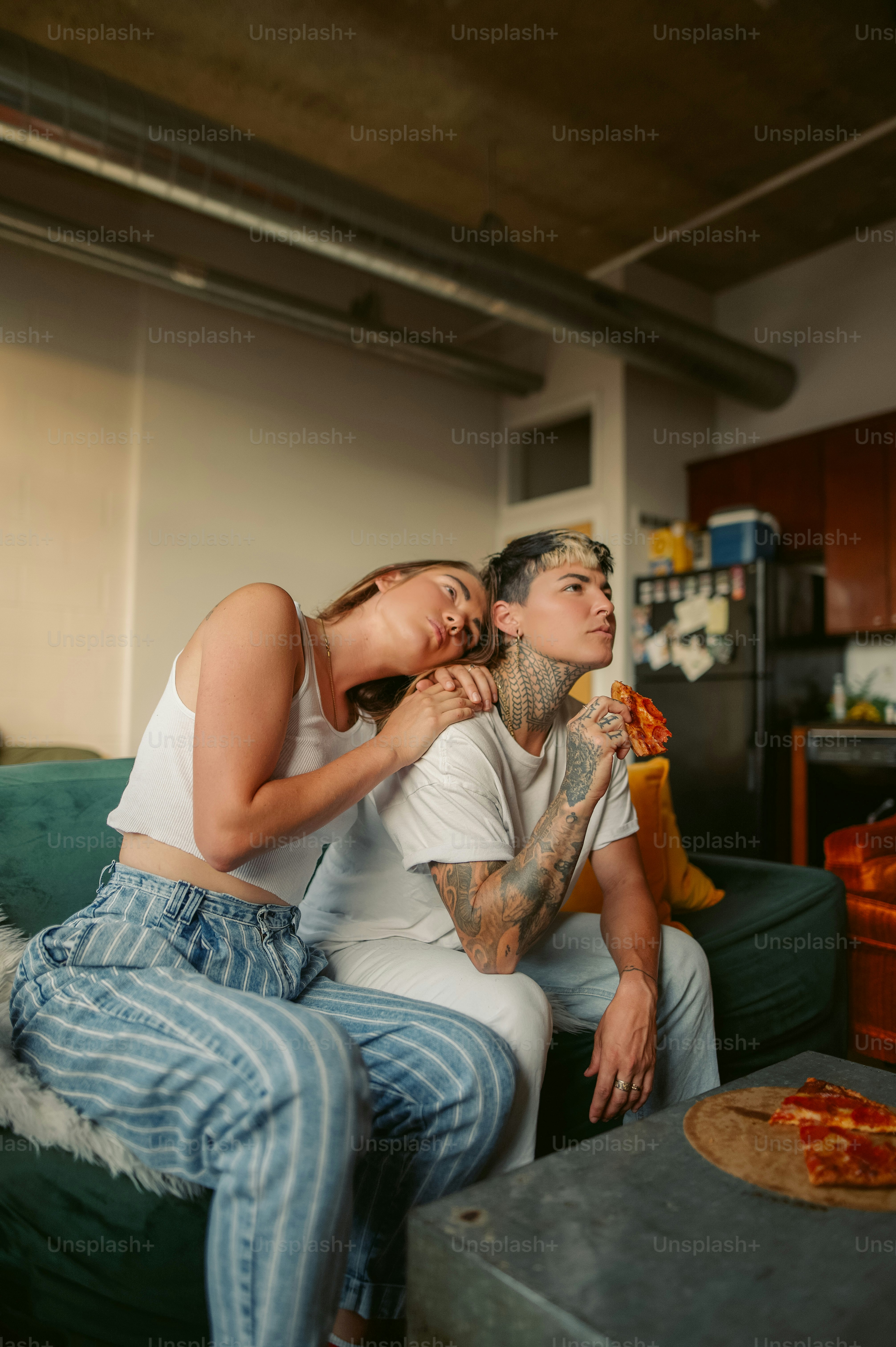 Un uomo e una donna seduti su un divano che mangiano pizza