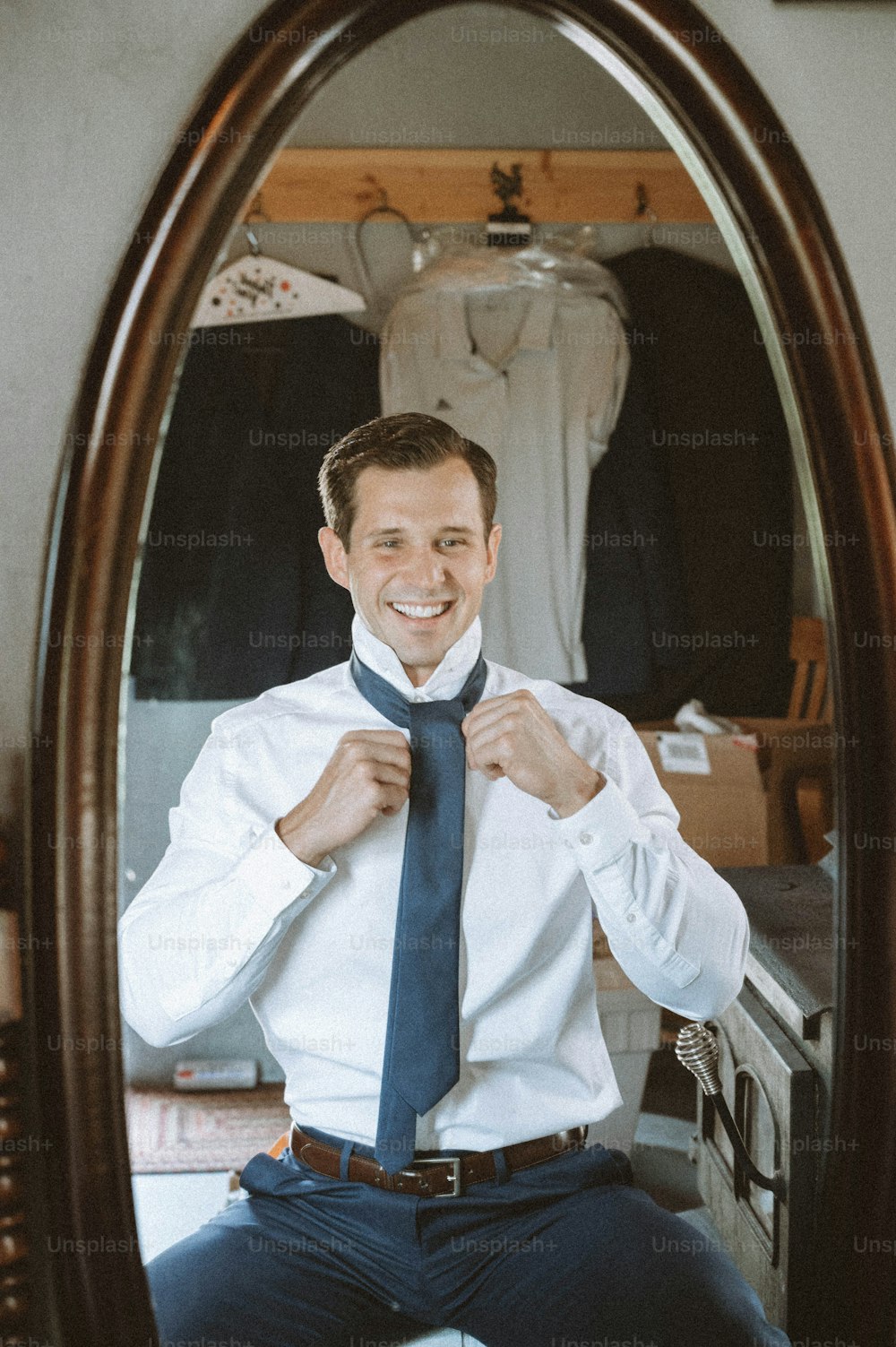 a man sitting in front of a mirror tying his tie