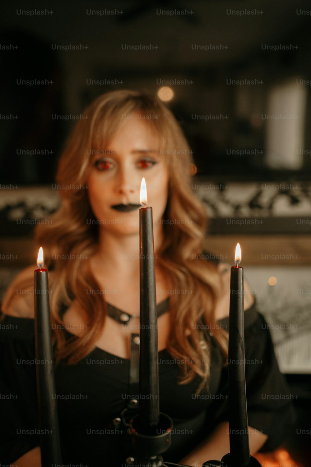 a woman with long hair and black makeup holding three candles