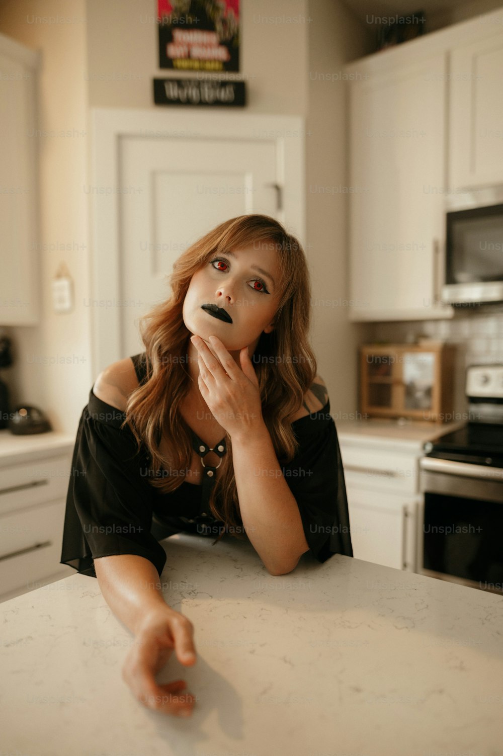a woman sitting at a kitchen table with a doughnut in her mouth