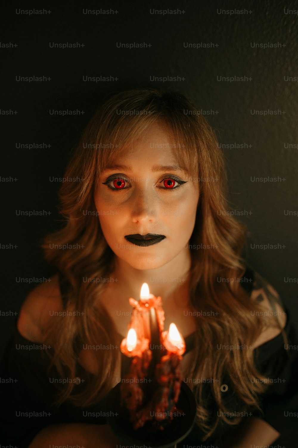 uma mulher com olhos vermelhos segurando uma vela acesa