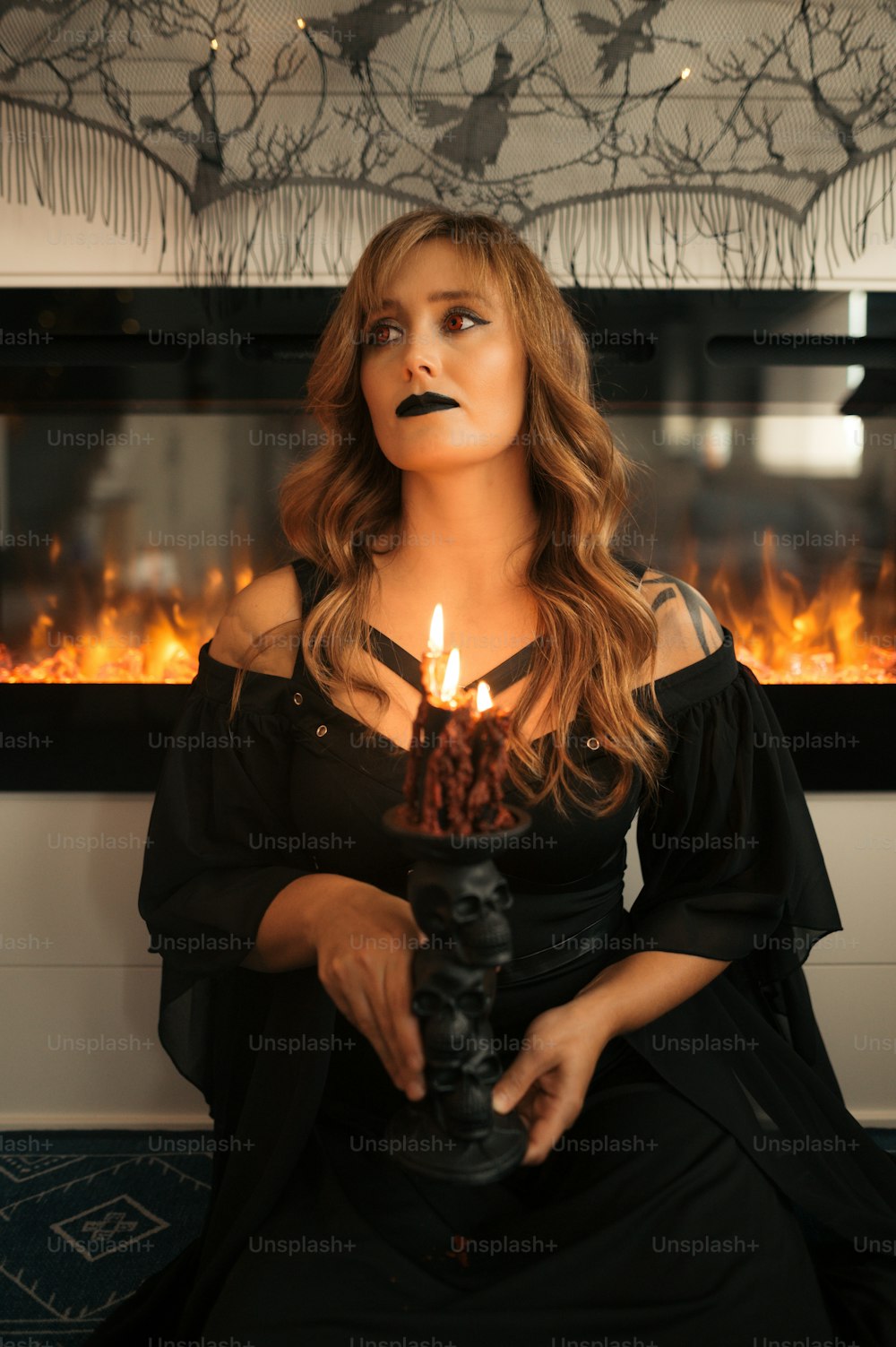 Eine Frau in einem schwarzen Kleid, die eine brennende Kerze hält
