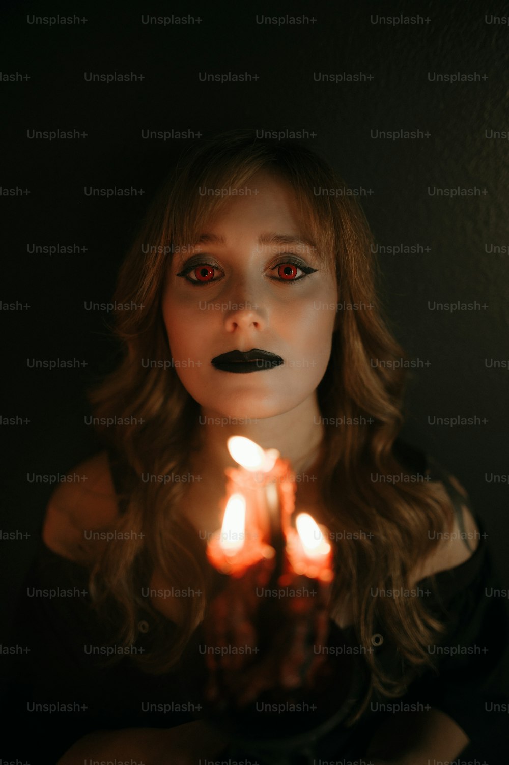 a woman with red eyes holding a lit candle