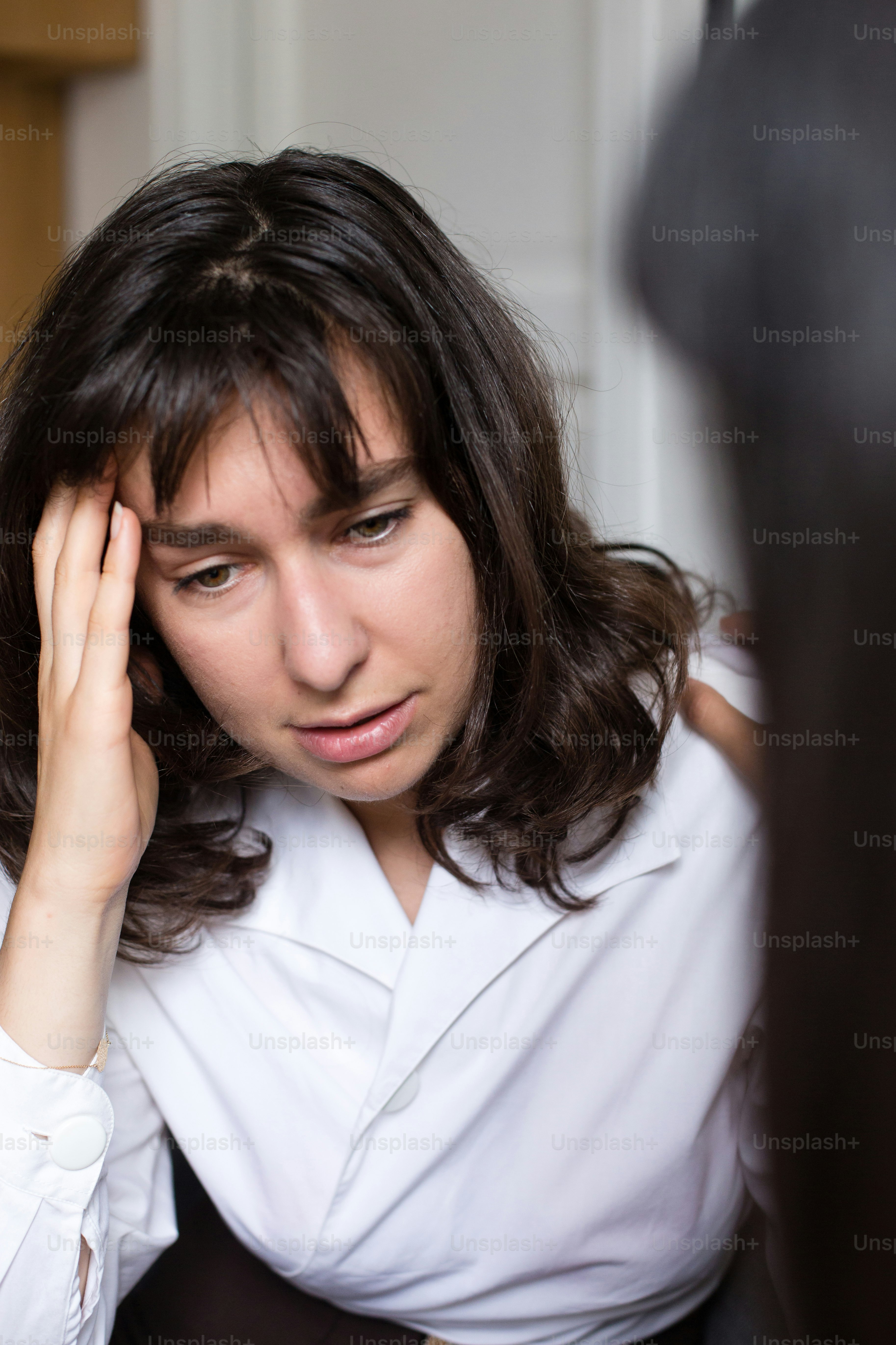 Une femme en chemise blanche portant sa main à sa tête
