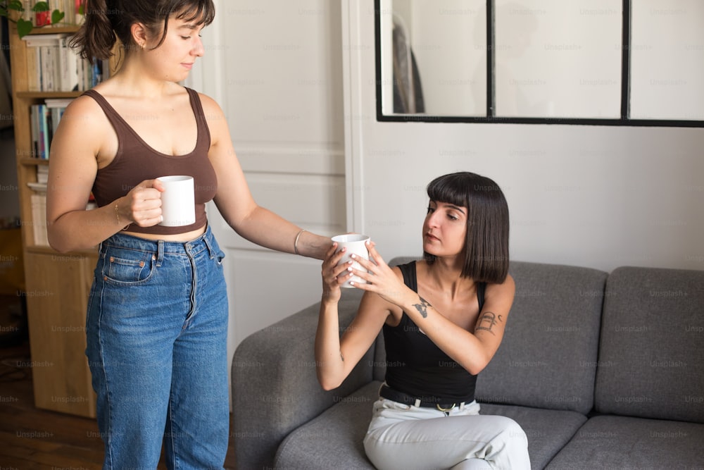 a woman sitting on a couch next to a woman holding a cup