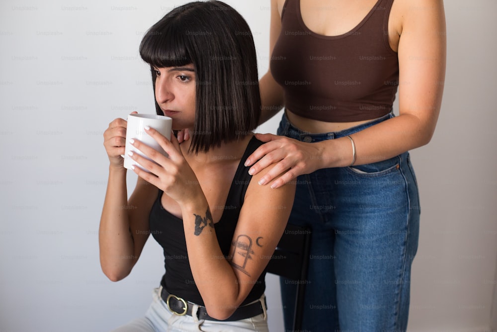 a woman holding a cup while another woman looks at her phone