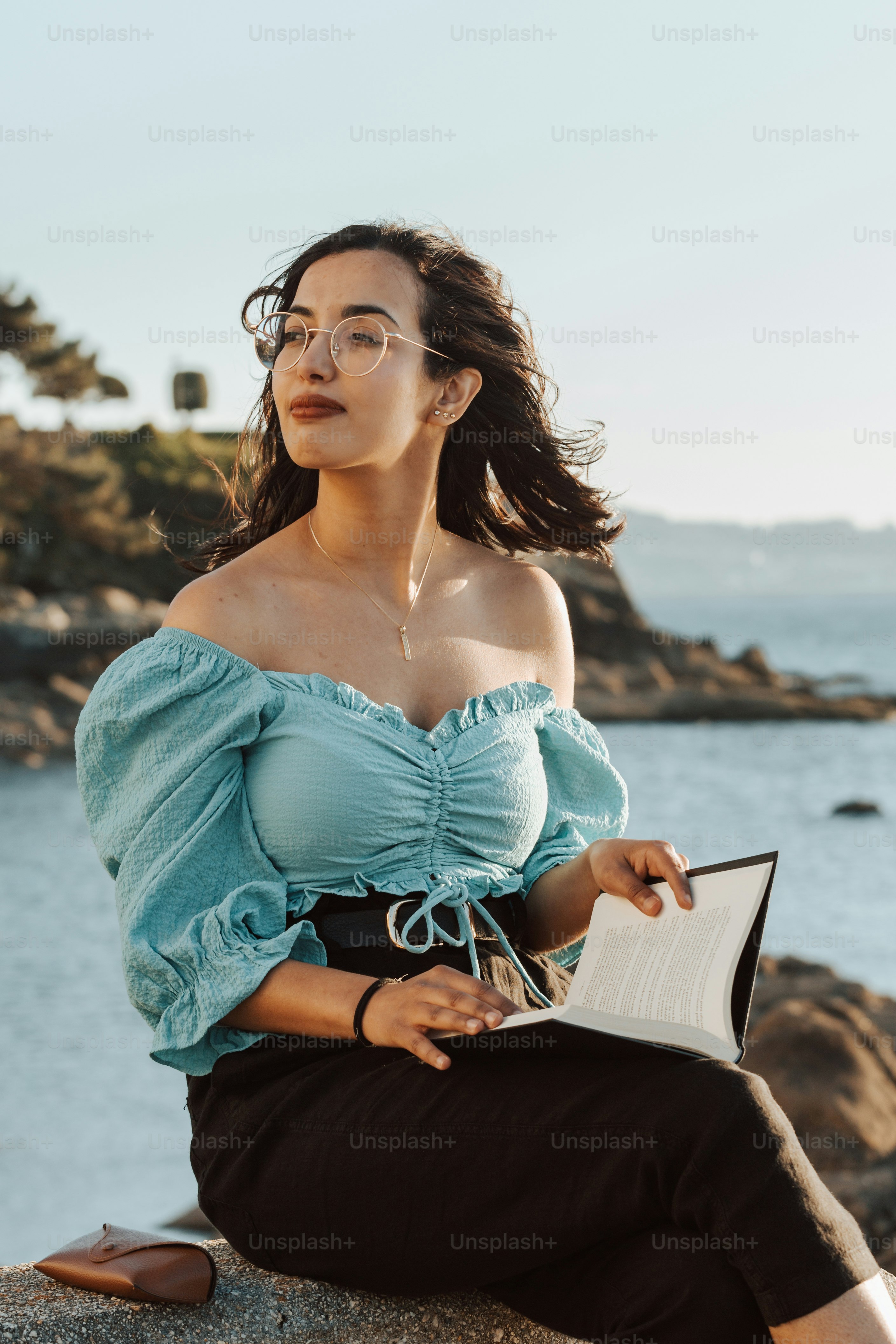 a woman sitting on top of a rock next to a body of water