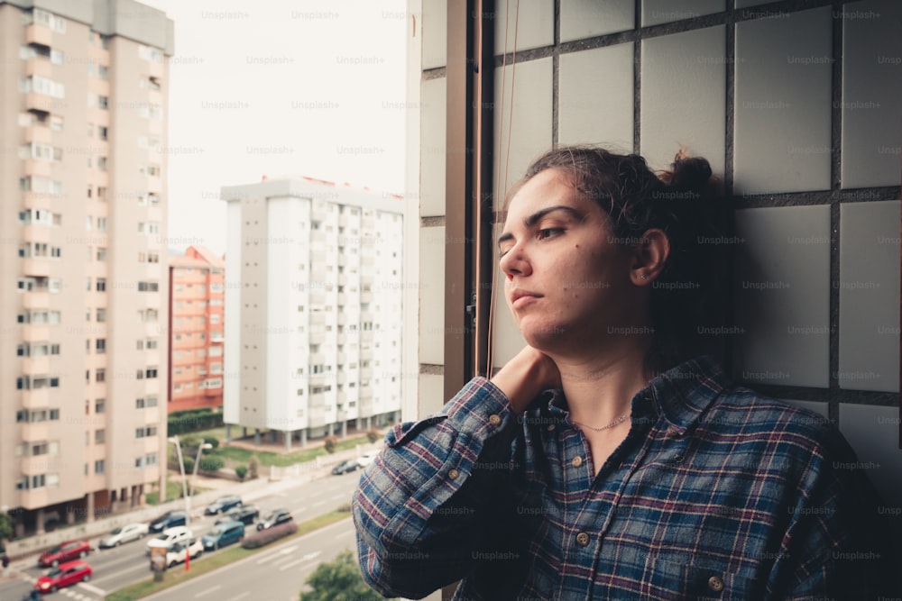 Una mujer apoyada contra una pared mirando por una ventana