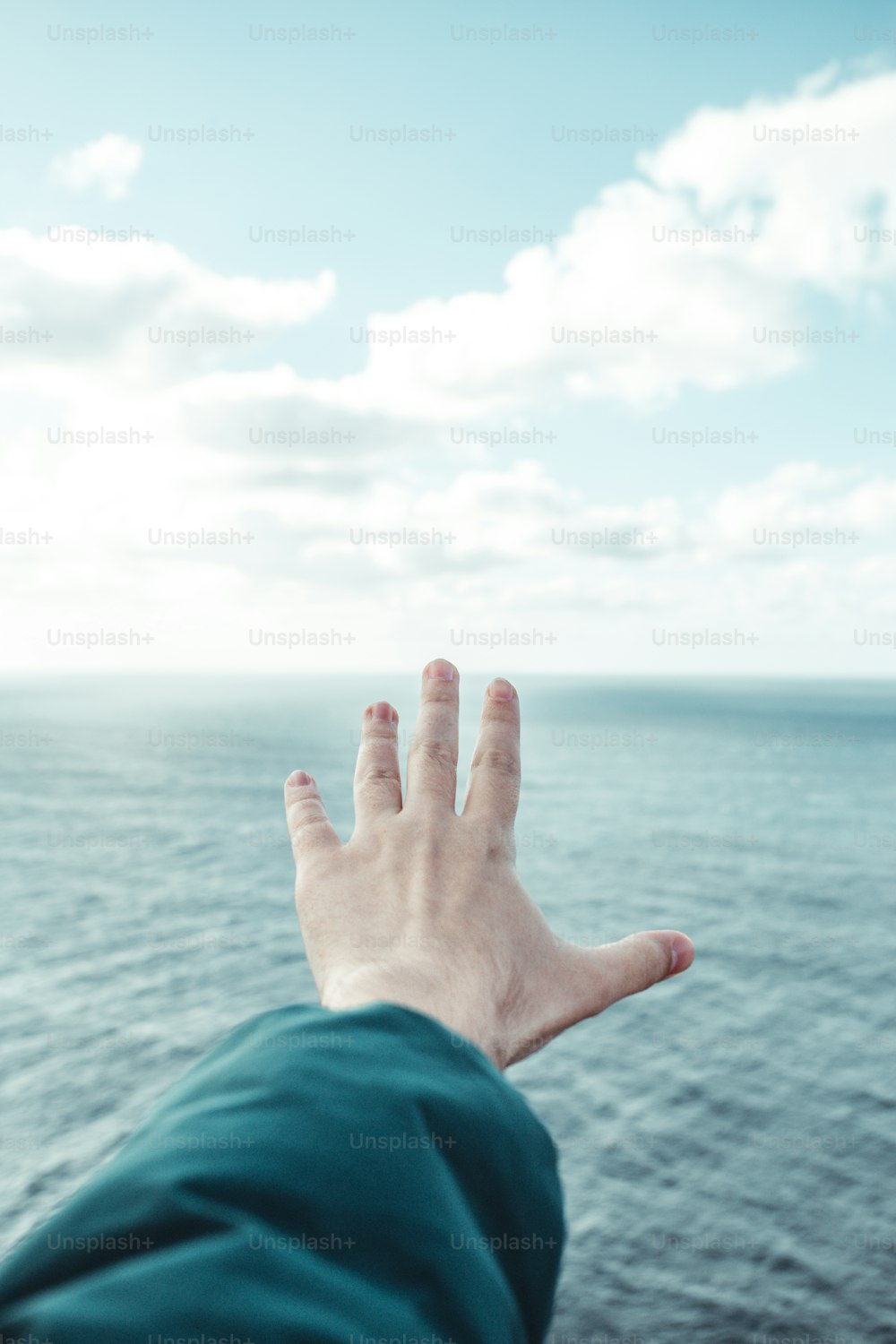 a person's hand reaching out towards the ocean