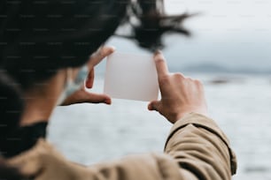 a person holding a white card in front of a body of water