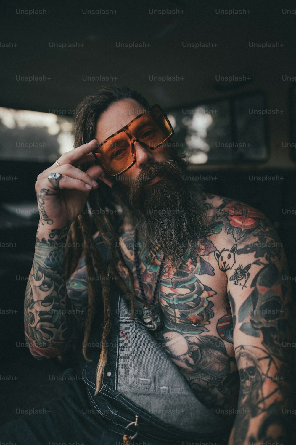 um homem com barba e tatuagens segurando um par de óculos escuros