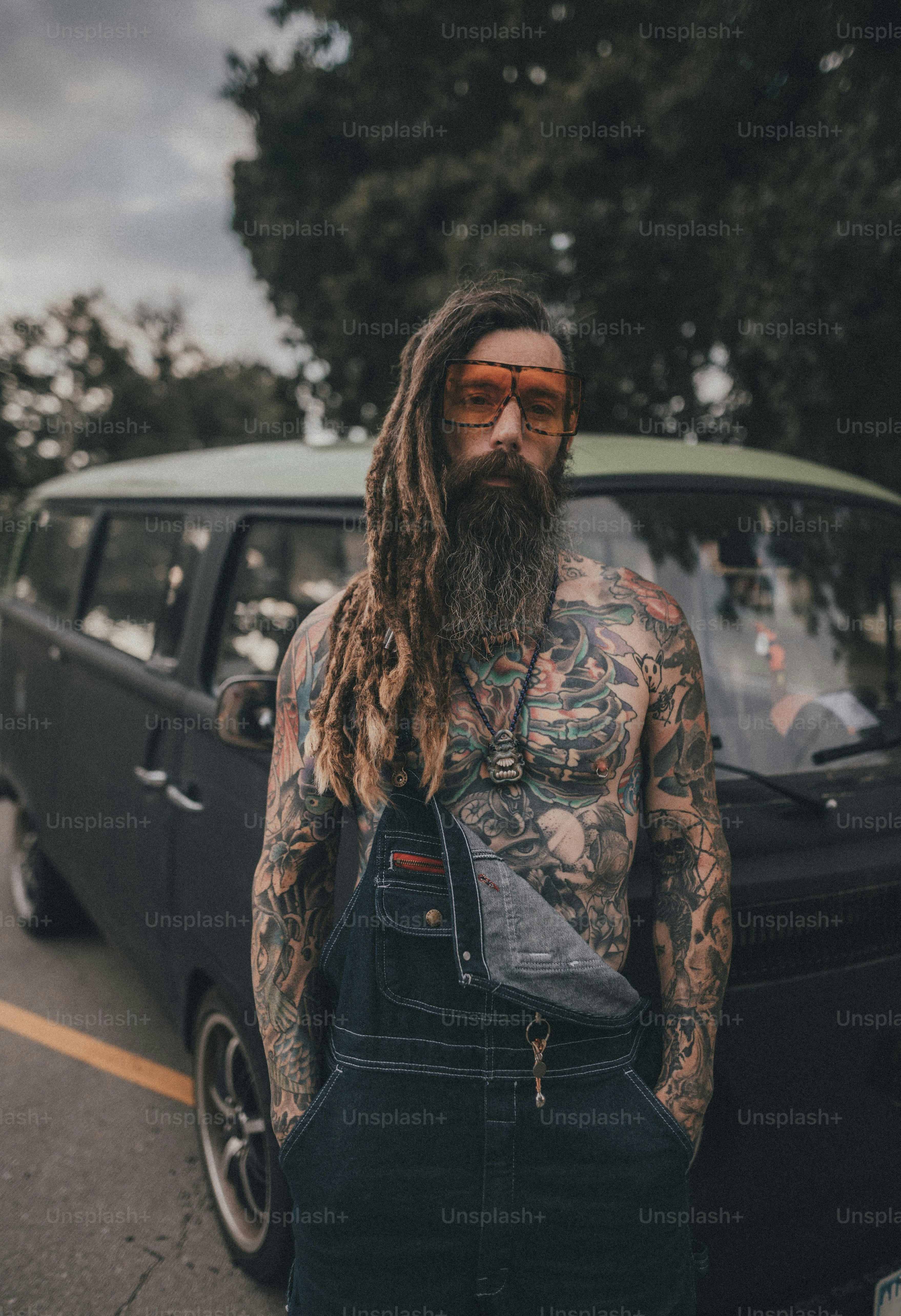 A man with a beard and tattoos standing in front of a car photo – New ...