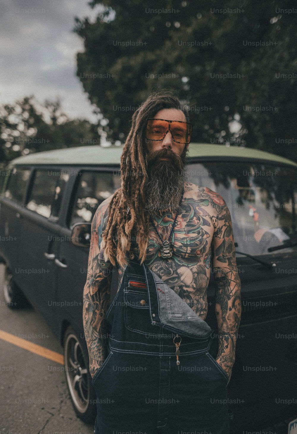 a man with a beard and tattoos standing in front of a car