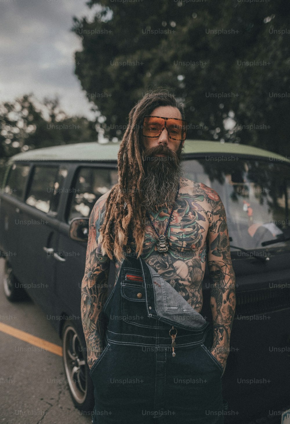 um homem com barba e tatuagens em pé na frente de um carro