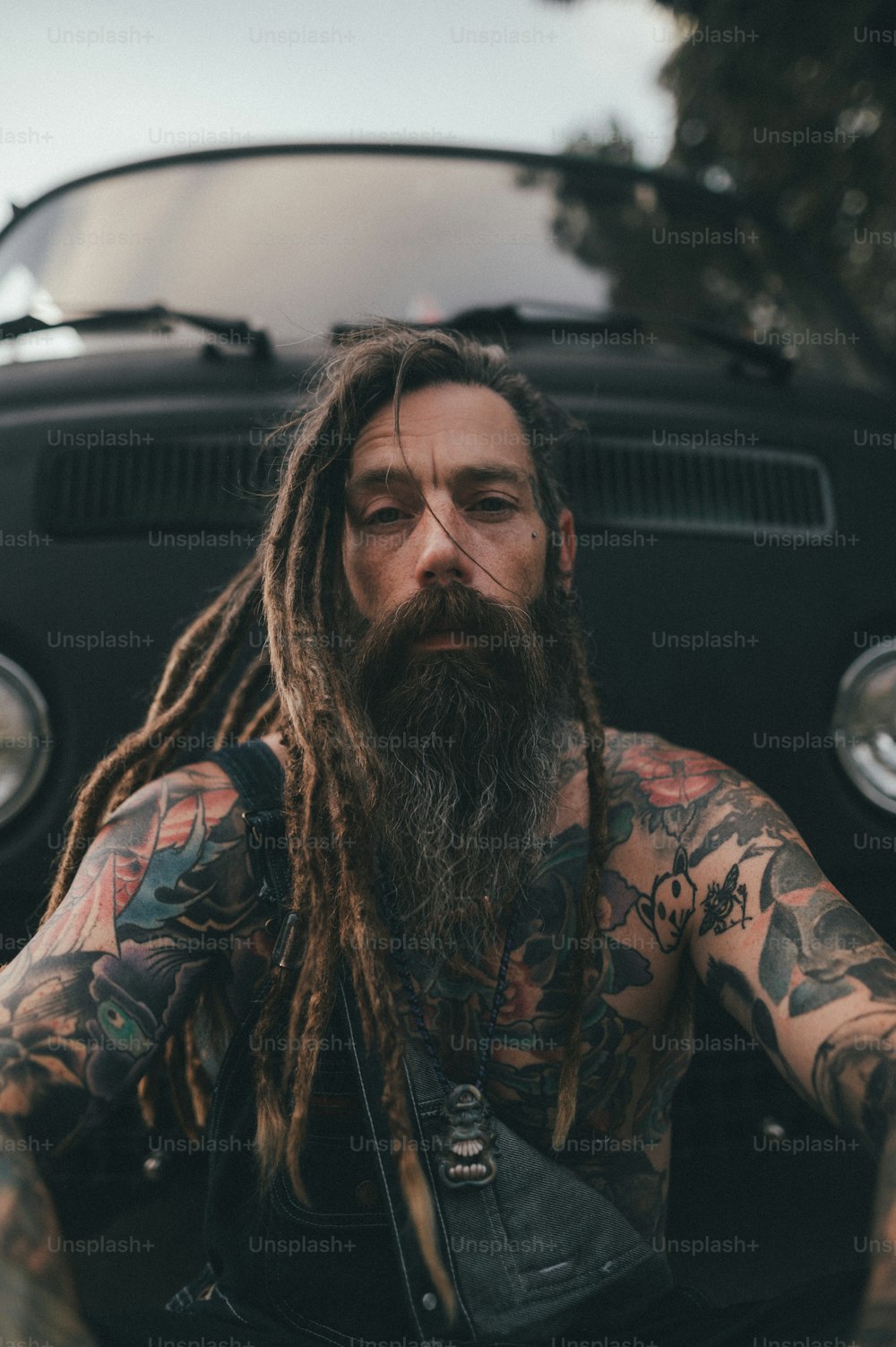 a man with long dreadlocks sitting in front of a car