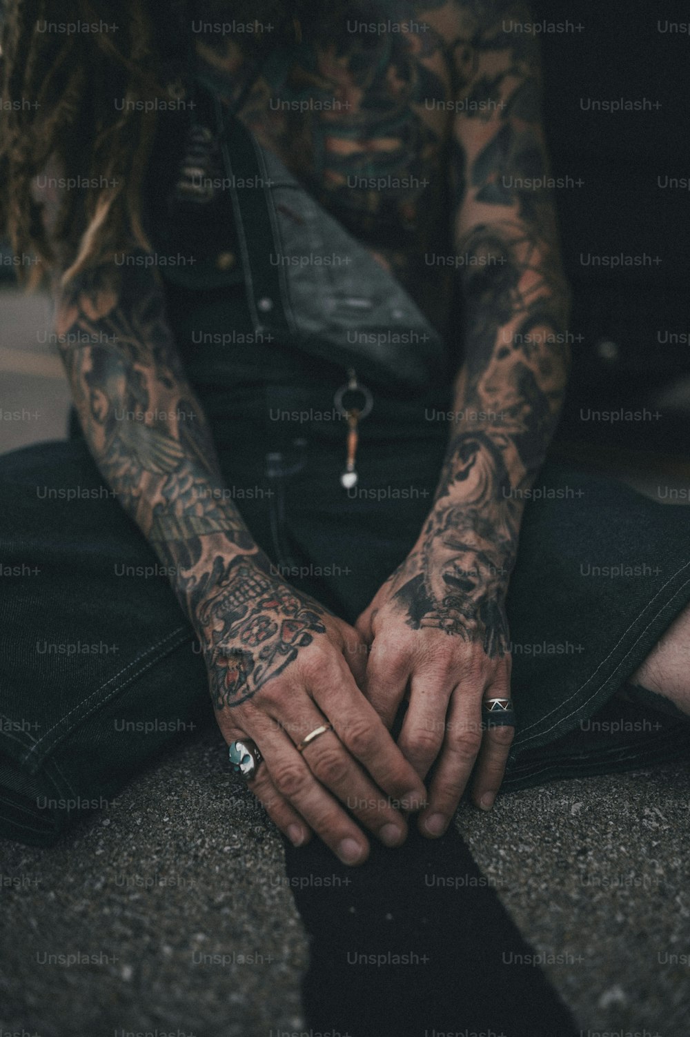 a tattooed man sitting on the ground holding his hands