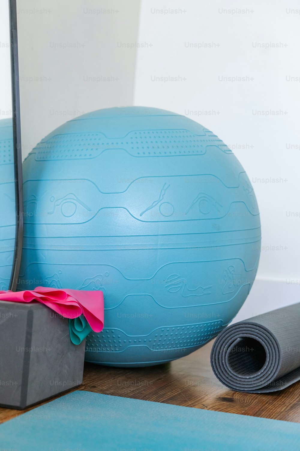 uma bola de exercício azul, tapete de ioga e bolsa de ginástica em um chão de madeira