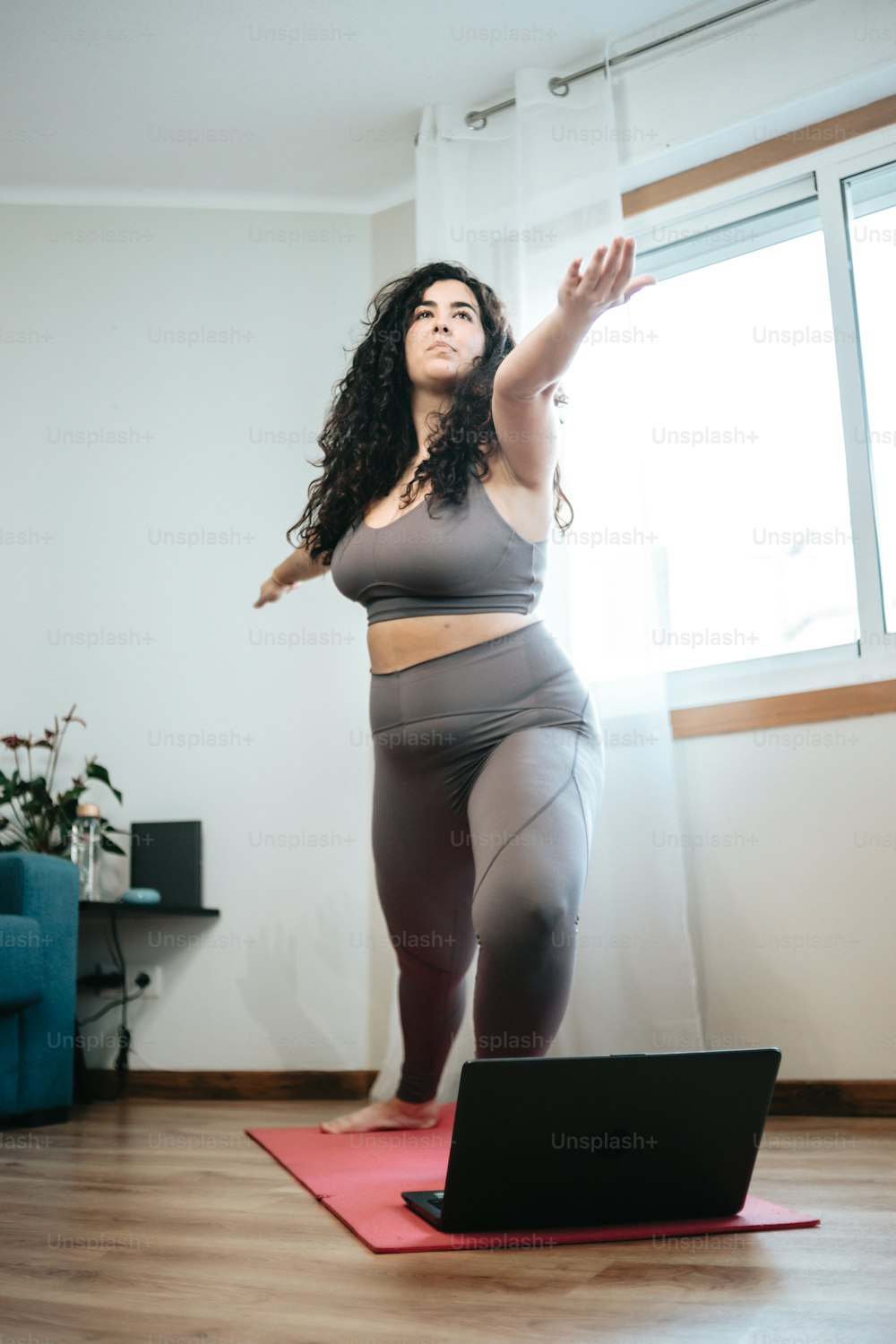 a woman standing on a yoga mat in front of a laptop