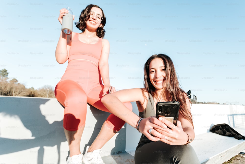 duas mulheres sentadas em uma parede com um celular