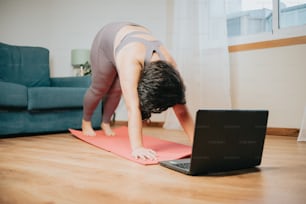 Una mujer haciendo yoga en una esterilla de yoga frente a una computadora portátil