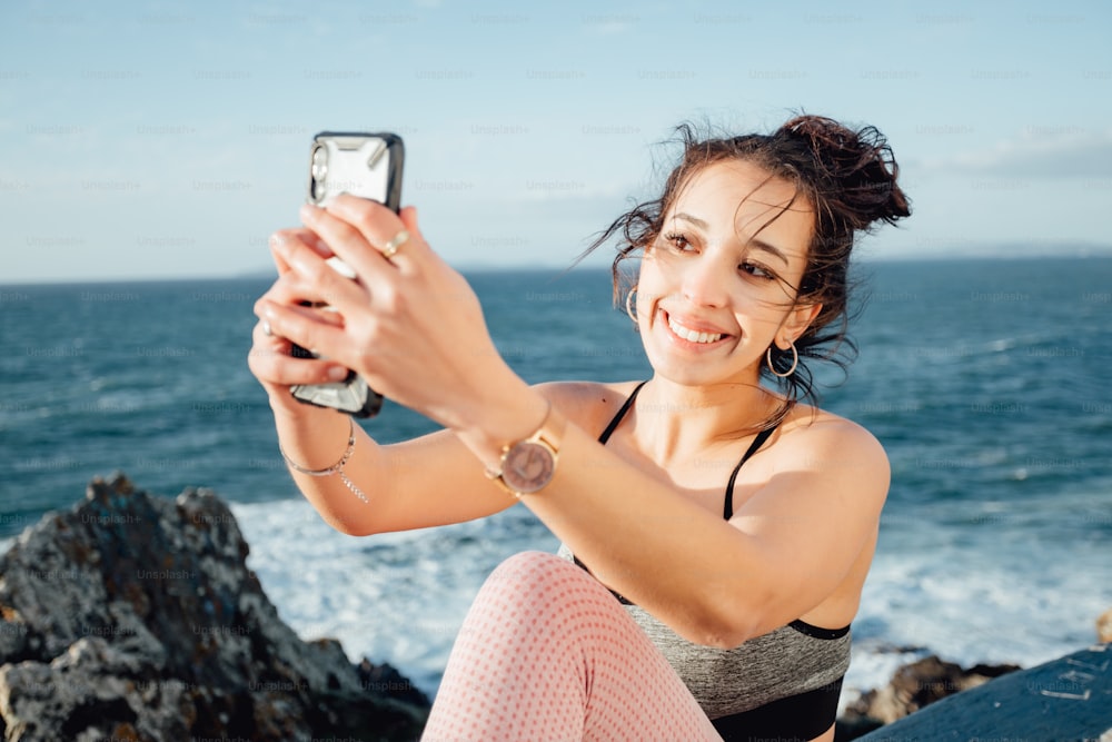 a woman sitting on a rock taking a picture with her cell phone