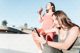 two women sitting on a ledge looking at a cell phone