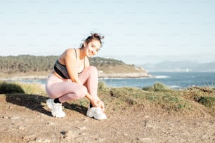 a woman squatting on a hill near the ocean