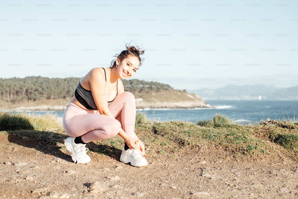 a woman squatting on a hill near the ocean