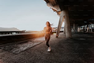 a woman running under a bridge at sunset