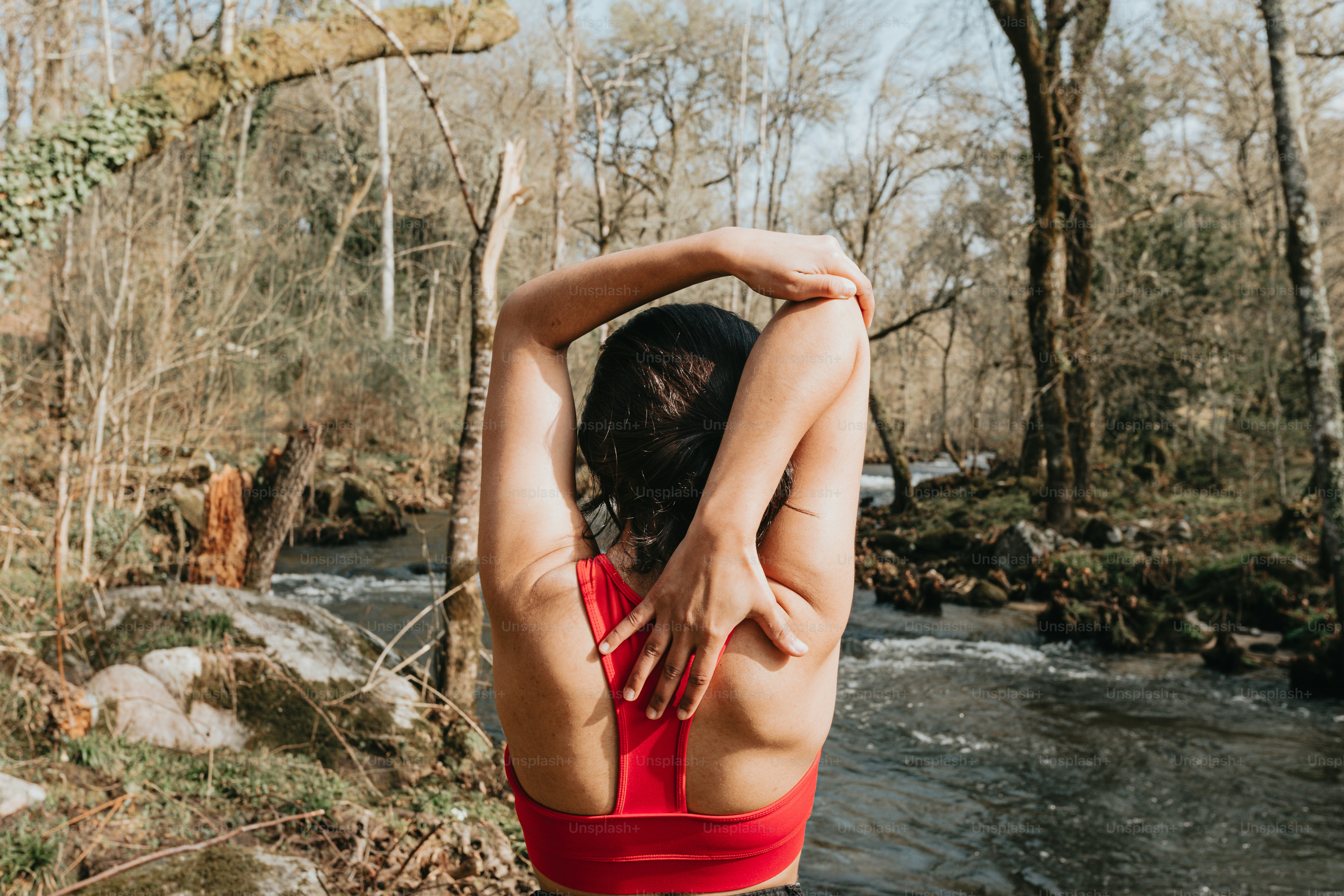 a woman in a red tank top standing in front of a river