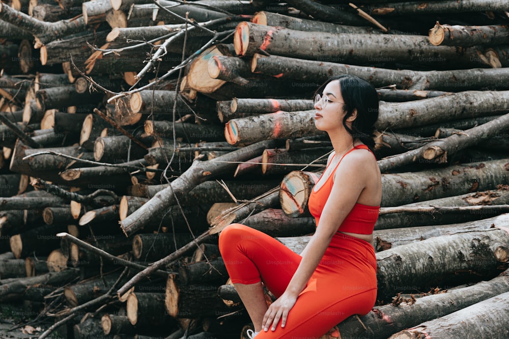 a woman in a red dress sitting on a pile of logs