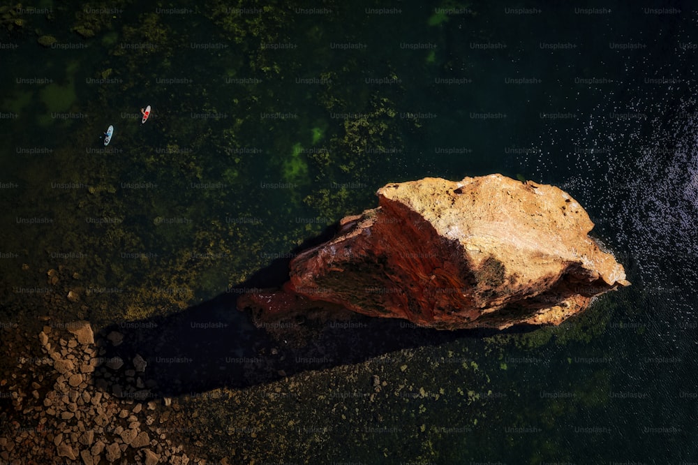 two people are swimming in the water near a large rock