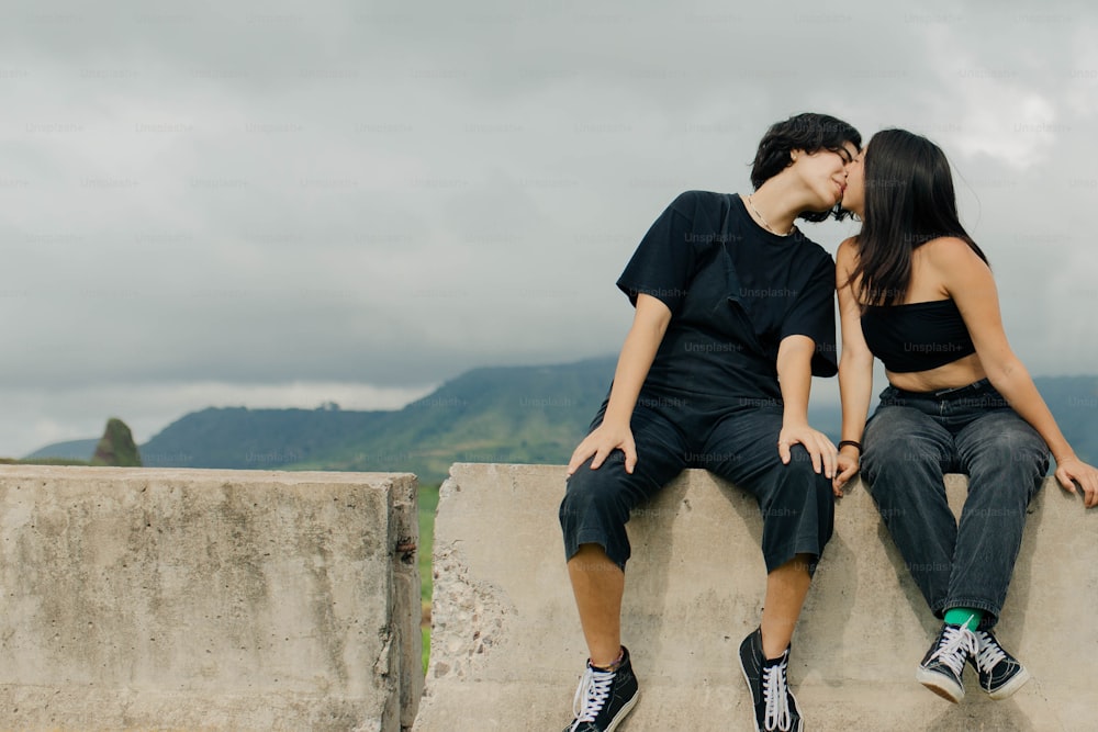 Un hombre y una mujer sentados en una pared besándose