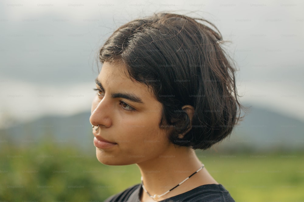 a young woman with a nose piercing looks off into the distance