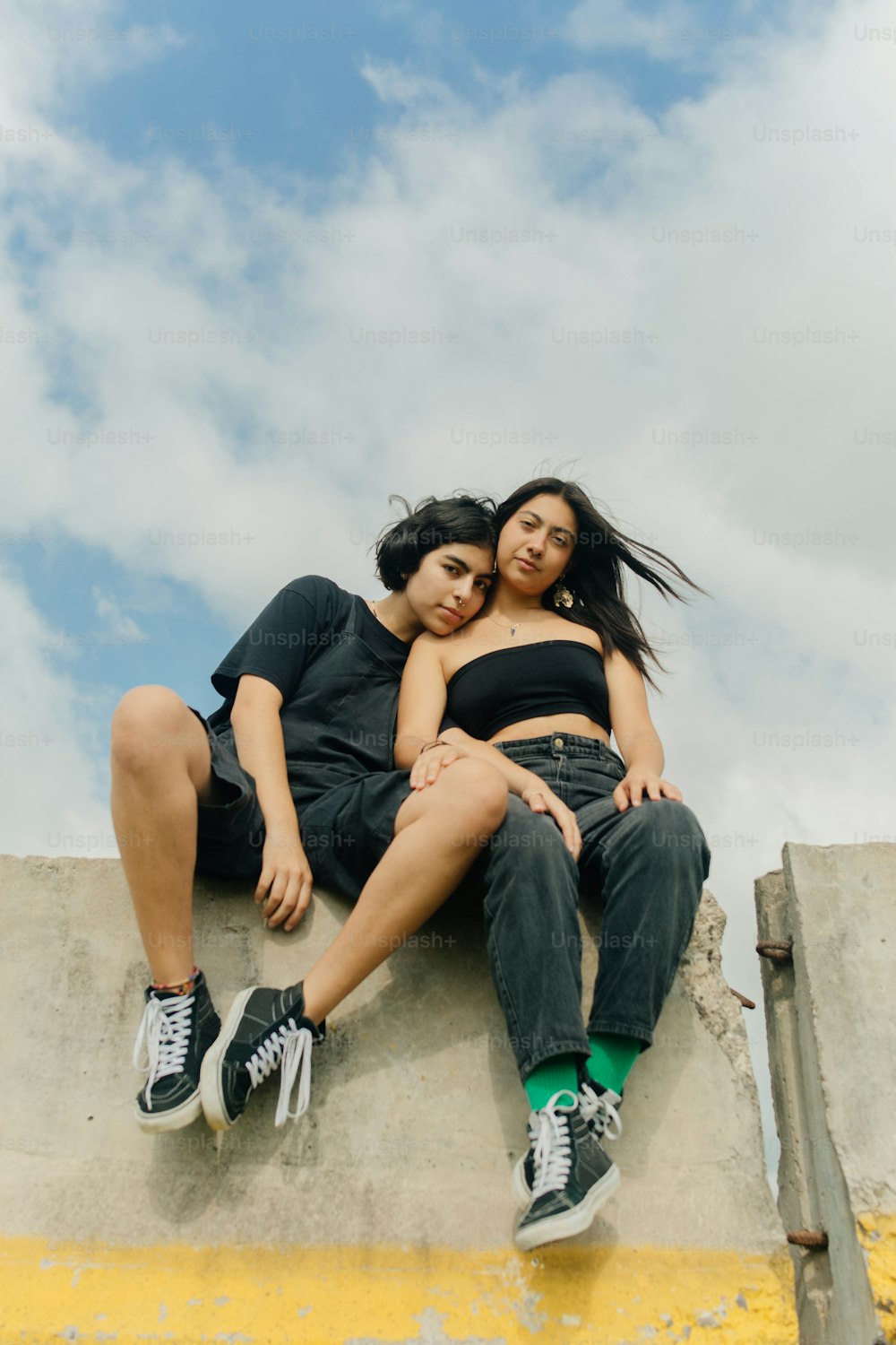 two young women sitting on a cement wall