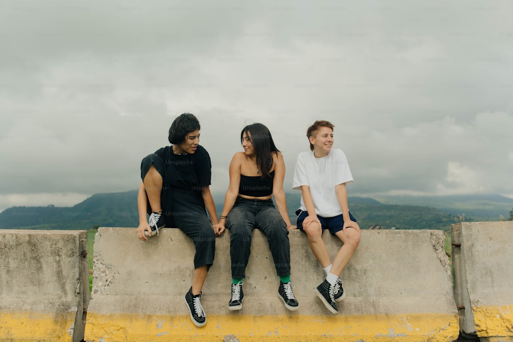 three people sitting on a ledge with mountains in the background