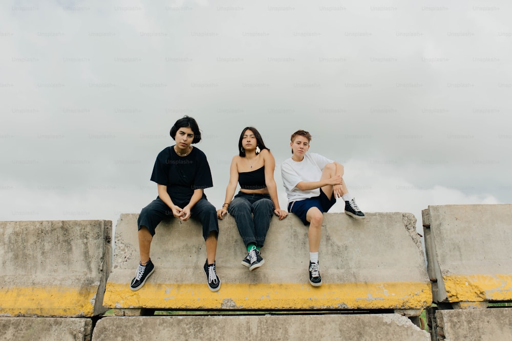 three people sitting on a cement wall