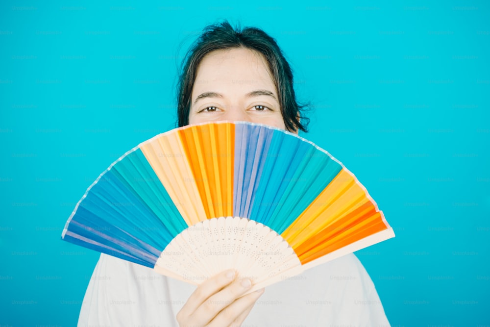 uma mulher segurando um ventilador colorido na frente de seu rosto