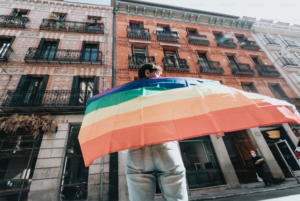 Un hombre sosteniendo un paraguas de colores del arco iris frente a un edificio