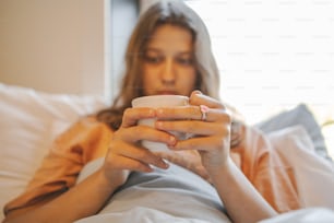 a woman laying in bed holding a cup of coffee