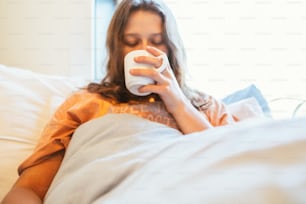 a woman laying in bed drinking from a cup