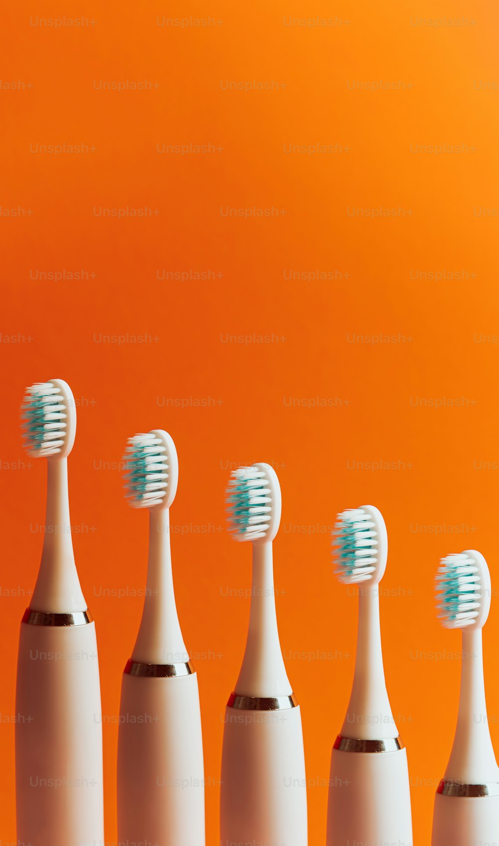 uma fileira de escovas de dentes elétricas sentada em frente a um fundo laranja