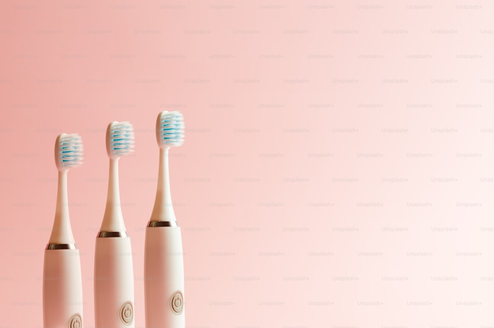 three electric toothbrushes on a pink background