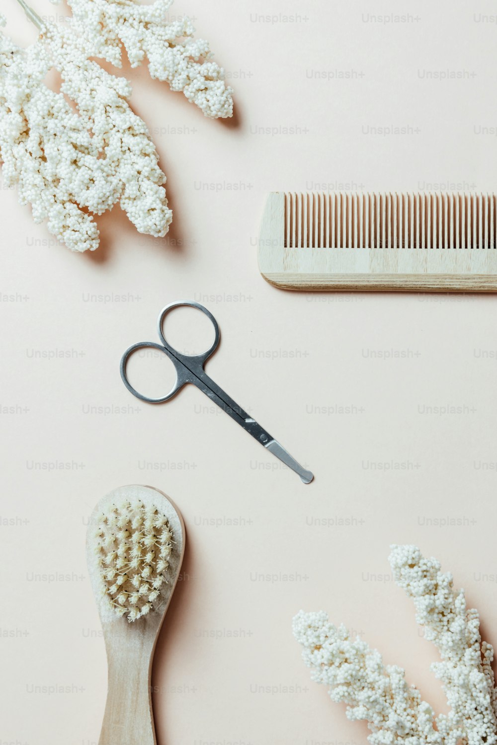 a pair of scissors, a comb, and pearls on a pink surface