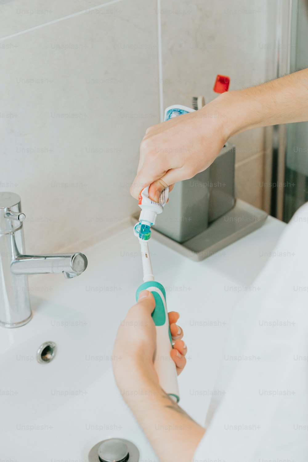 uma pessoa segurando uma escova de dentes em uma pia de banheiro